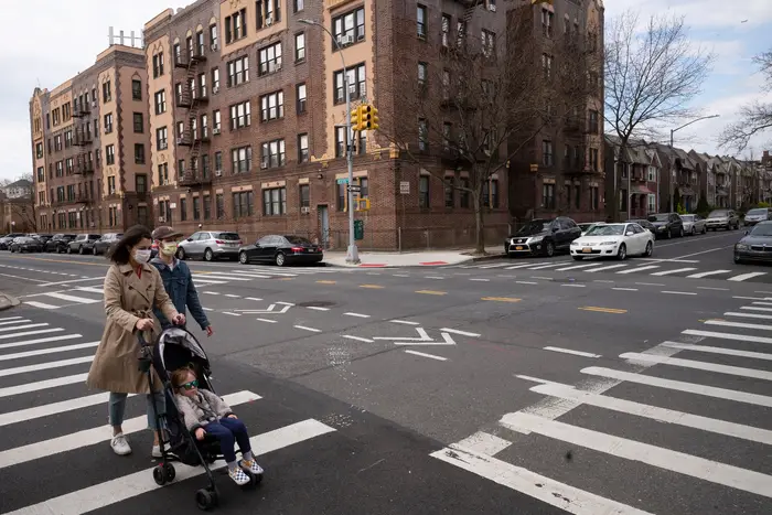 Couple wear masks during the coronavirus pandemic as they walk with their child through the intersection of Sterling St. and Bedford Ave., in the Prospect Lefferts Gardens neighborhood of New York.
